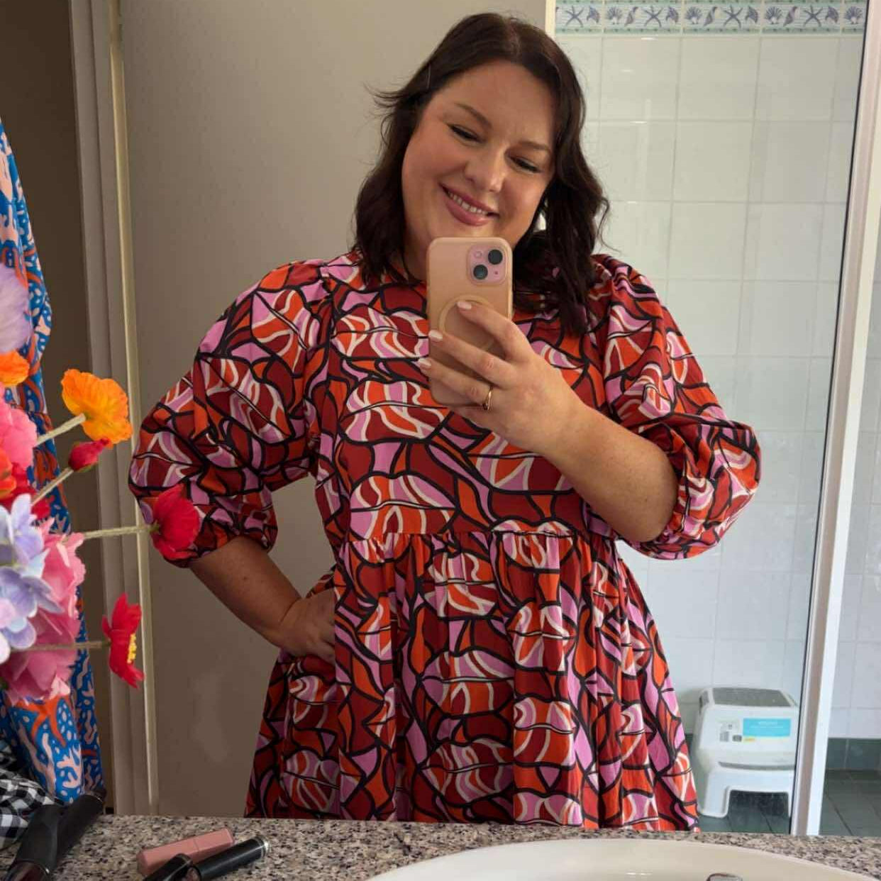 Person taking a mirror selfie wearing a red patterned dress in a bathroom.
