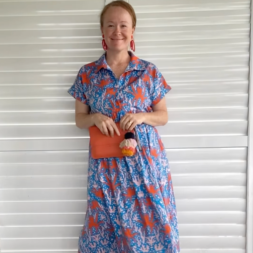 Woman wearing a colorful dress standing in front of white shutters.