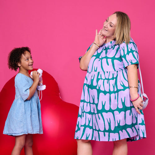 Two women, one adult and one child, standing against a pink background with a red heart-shaped object.