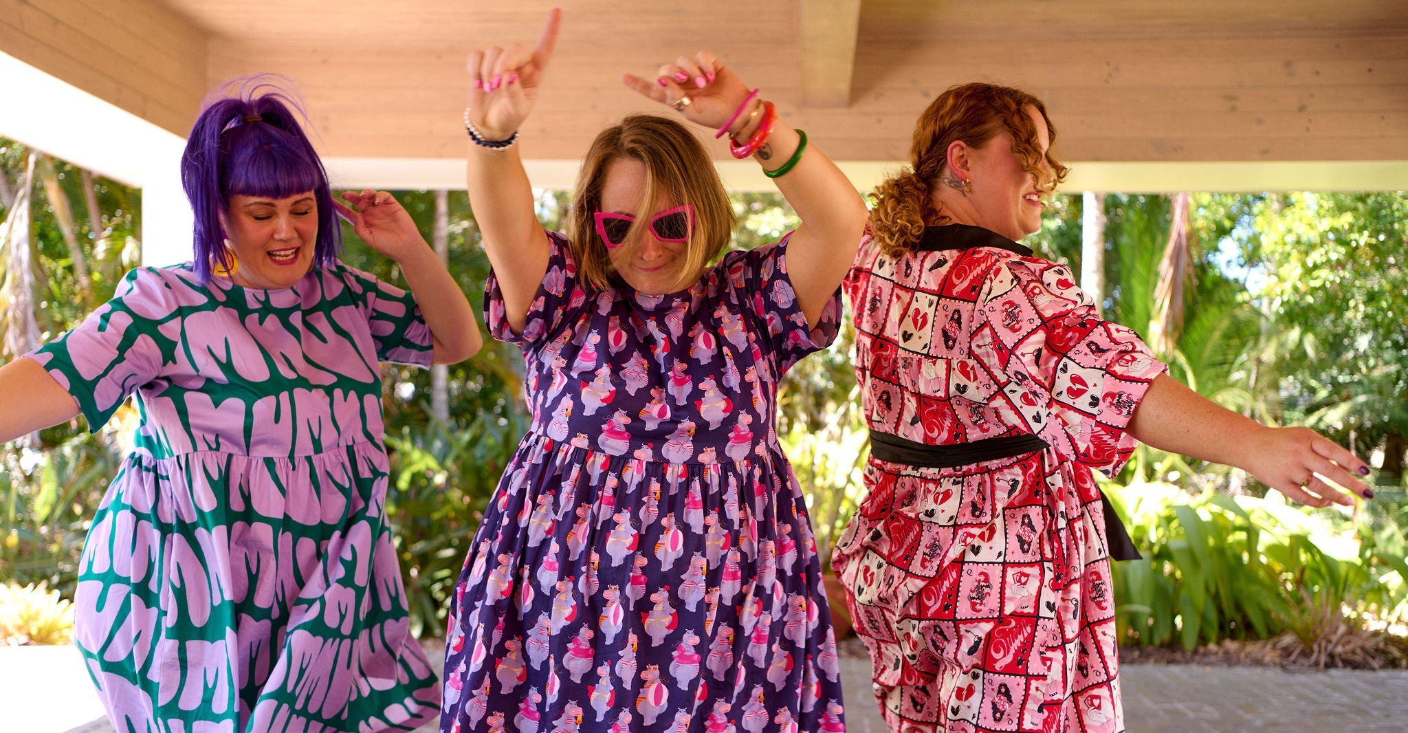 Three women in patterned dresses posing outdoors with trees in the background