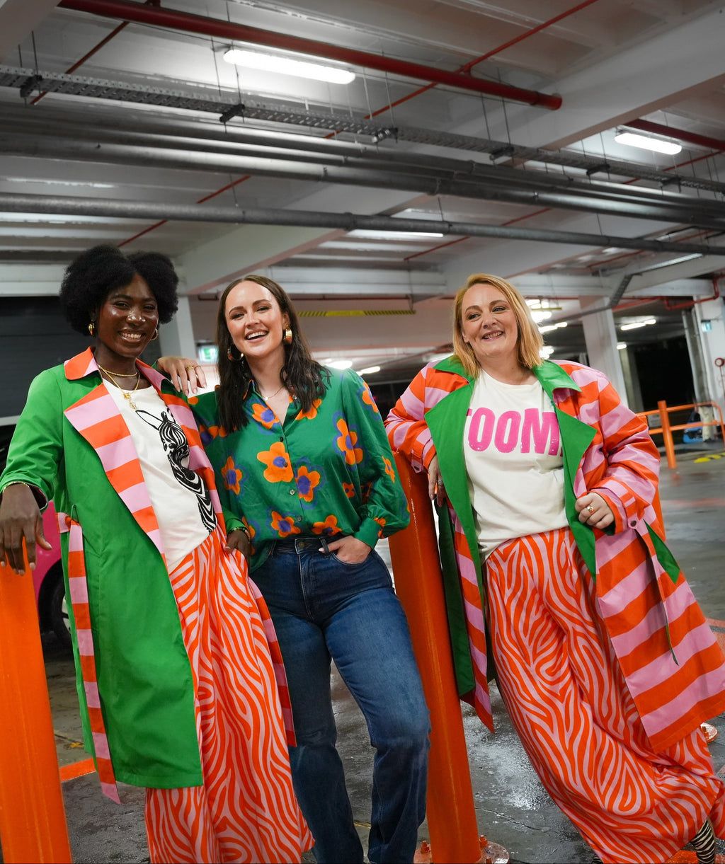 Three women posing in a parking garage with a pink car in the background.