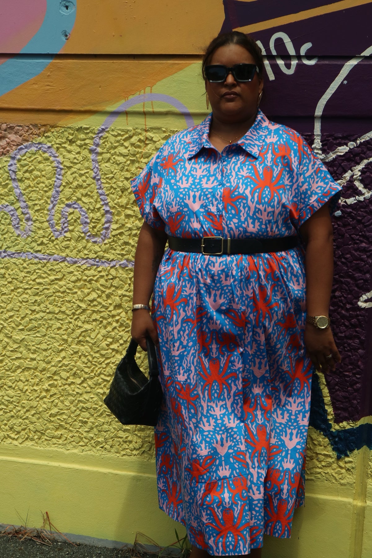 Toomi Octopus Friends dress, full length, worn with a black belt and sunglasses against a graffiti wall