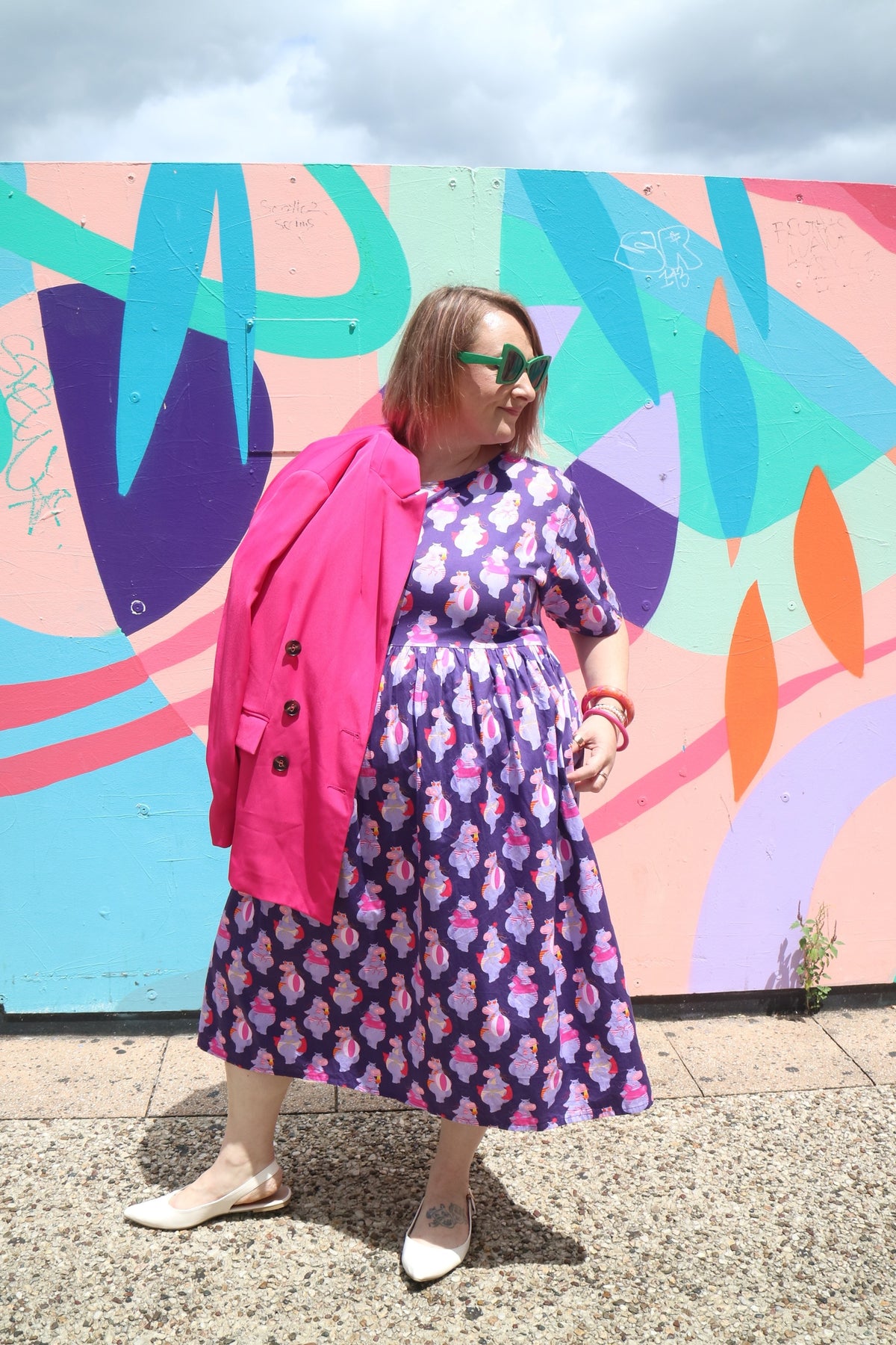 Toomi Tess The Hippo dress worn with a pink cardigan against a bright painted mural