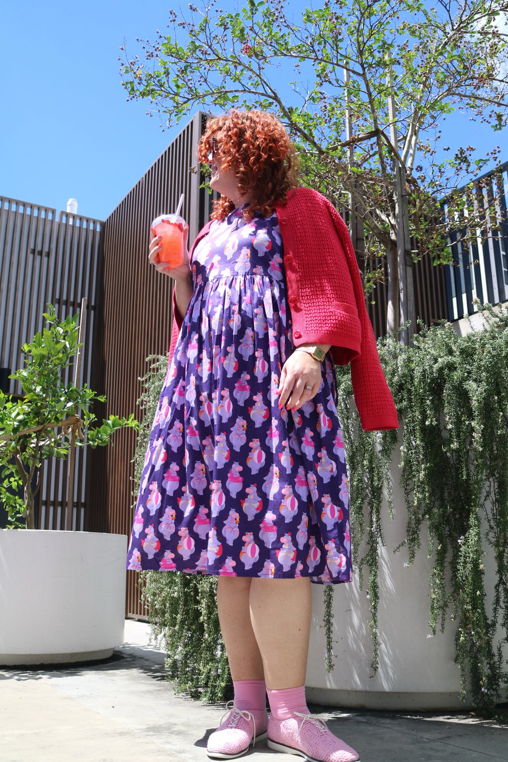 Toomi Tess The Hippo dress, full length outdoors, worn with a red cardigan and pink shoes